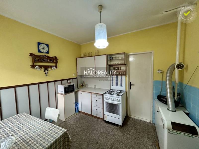 Konyha egy családi házban sárga falakkal, fehér bútorokkal és szőnyegpadlóval.