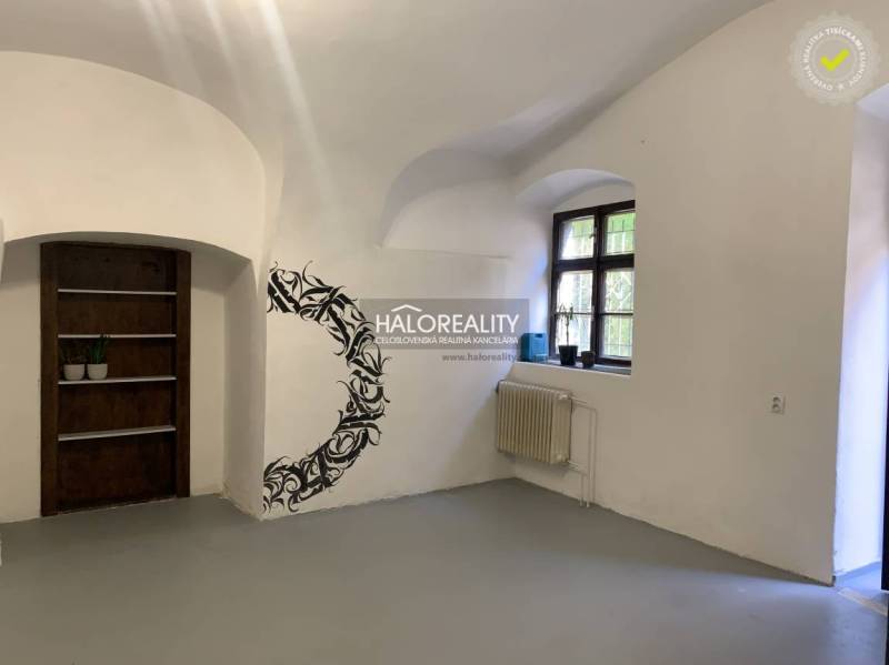 Egy fehér falú, ablakkal, fali dekorációval és fa polccal rendelkező iroda belső tere.