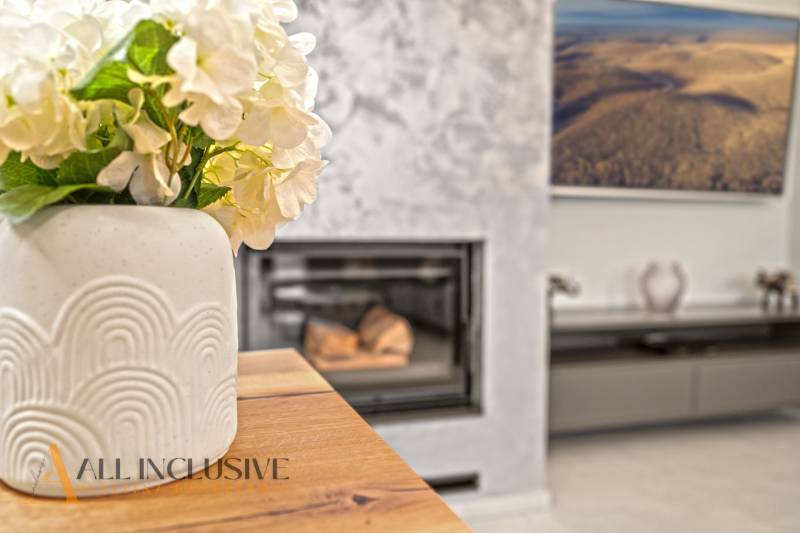 Váza virágokkal az asztalon, fa dekorációjú padló, kandalló a családi házban.