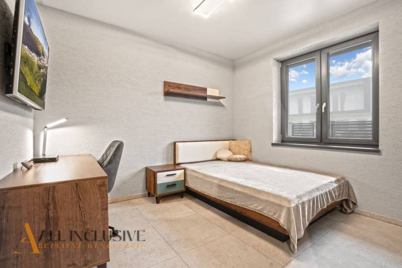 Hálószoba családi házban egyszerű berendezéssel, íróasztallal és kényelmes ággyal.