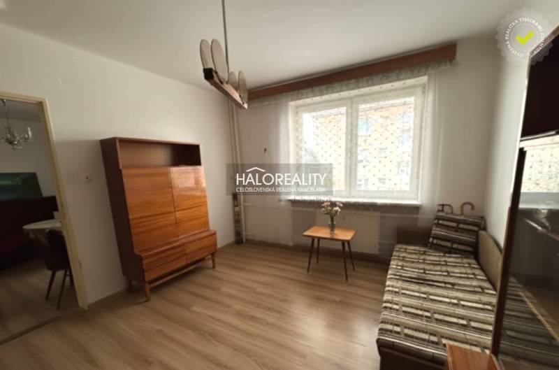 Nappali egy háromszobás lakásban, fa dekor padlóval, kanapéval, szekrénnyel és ablakkal.