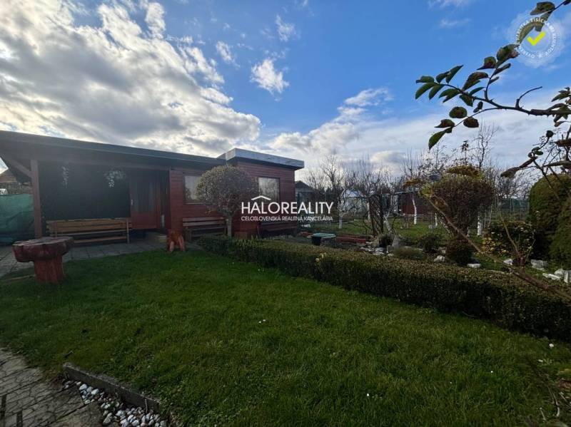 Fából készült pavilon a kertben Iglón, zöld gyep és növényzet mellett.