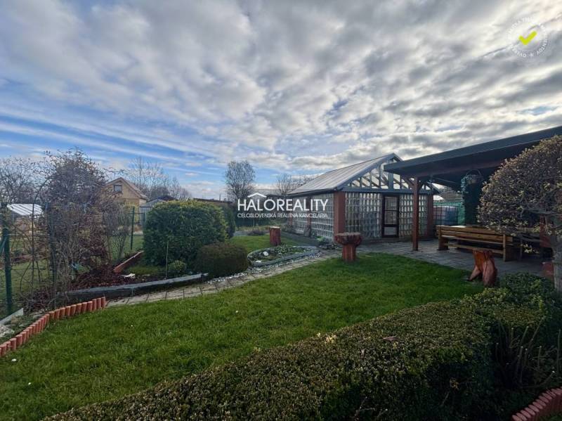 A Szepesújvár kertjei gondozott bokrokkal, gyepes területtel és fa pavilonnal.