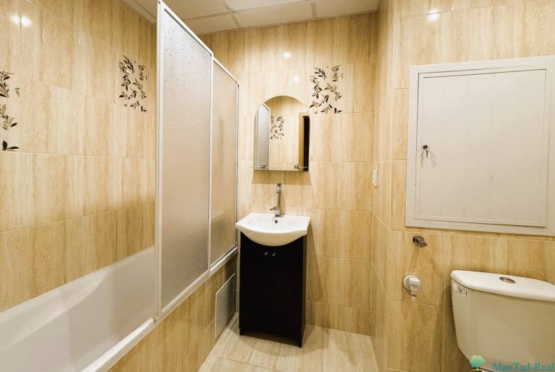 Fürdőszoba káddal, mosdóval és WC-vel egy háromszobás lakásban világos csempékkel.