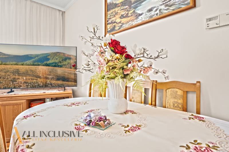 Étkező egy családi házban, virágdíszítéssel az asztalon és televízióval a háttérben.