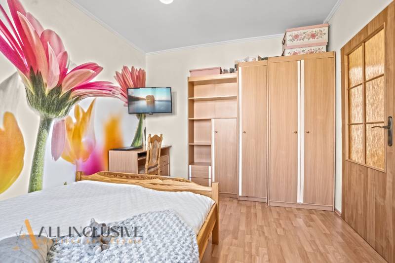 Hálószoba családi házban virágos tapétával, fa dekor padlóval és bútorokkal.