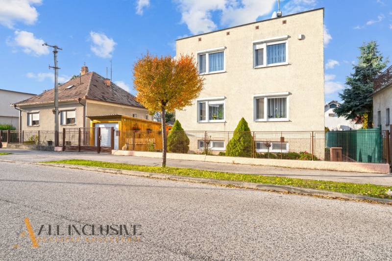 Családi házak Dunaszerdahelyen, fákkal szegélyezett utcák, rácsos kerítések, kék ég.