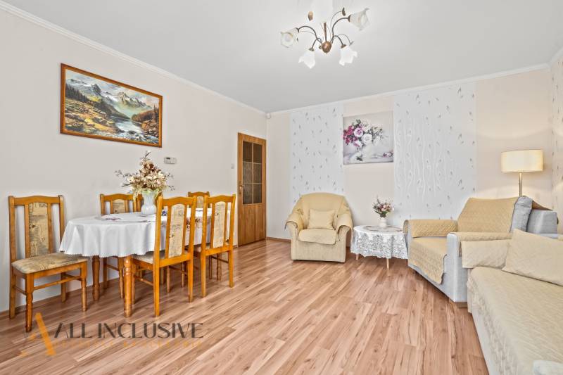 Nappali egy családi házban, fa mintázatú padló, étkezőasztal, fotelek, képek.