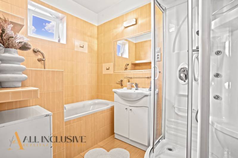 Fürdőszoba családi házban káddal, zuhanyzóval és tükörrel az okkersárga csempéken.