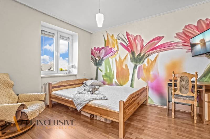 Hálószoba egy családi házban színes virágos tapétával és fa dekorációjú padlóval.