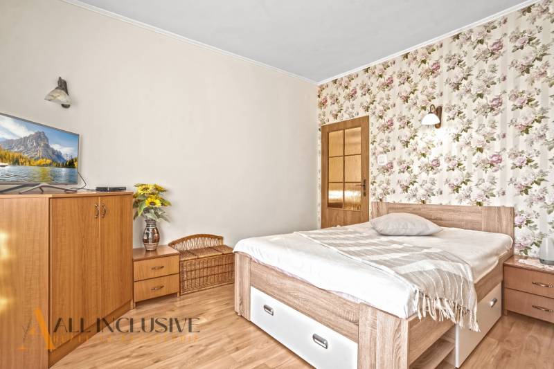 Hálószoba családi házban virágos tapétával, televízióval és fa dekorációjú padlóval.