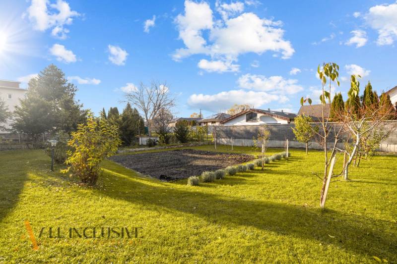 Családi ház kertje Dunaszerdahelyen gyepfelülettel, fákkal és rendezett virágágyással.