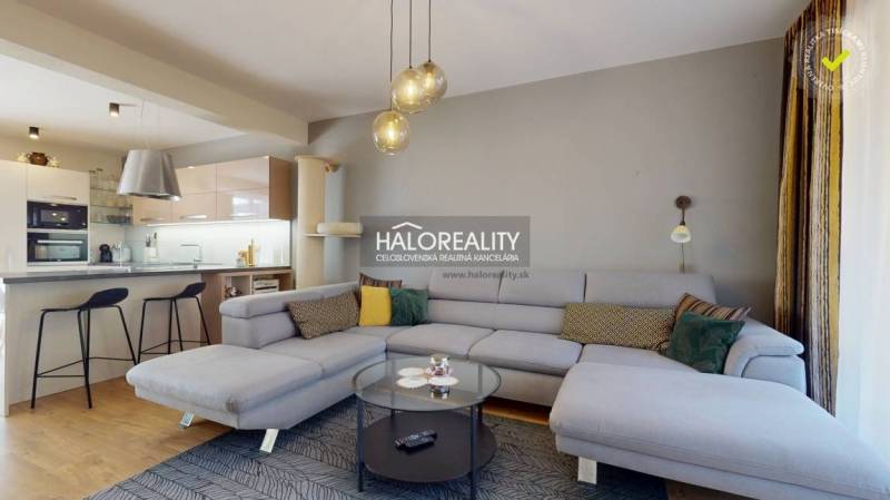 Tágas nappali egy családi házban kanapéval, konyhasarokkal és fa dekorációjú padlóval.