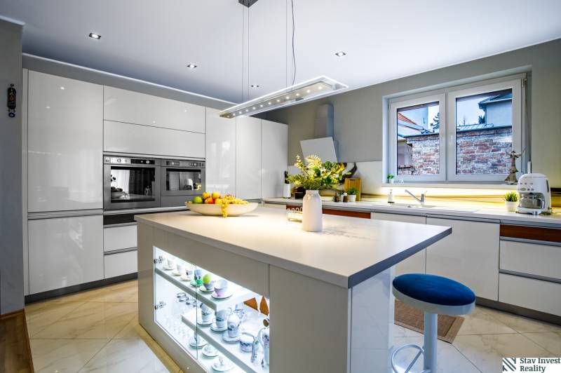 Konyha családi házban központi szigettel, fehér szekrényekkel és készülékekkel.