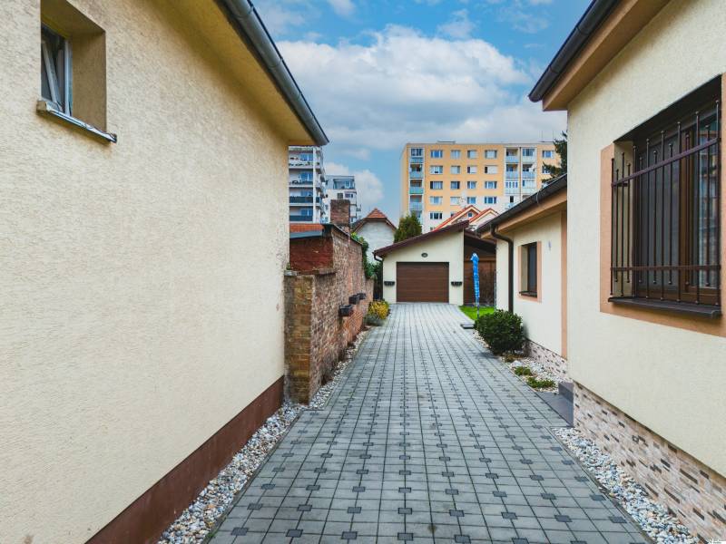 Kilátás egy családi ház udvarára a Szkolská utcából Szencen, járdával és bokrokkal.