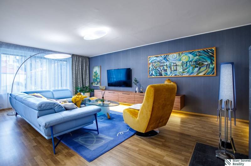 Nappali egy családi házban kék kanapéval, sárga fotellel és fa dekoros padlóval.