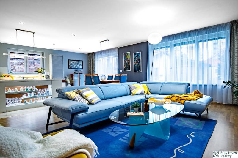 Nappali egy családi házban kék kanapéval, üvegasztallal és fa mintázatú padlóval.