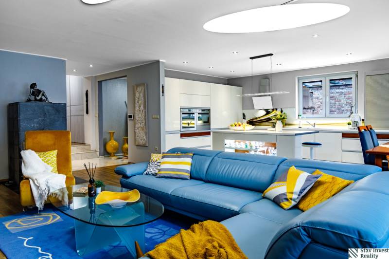 Nappali egy családi házban kék kanapéval és konyhával, fa hatású padlóval.