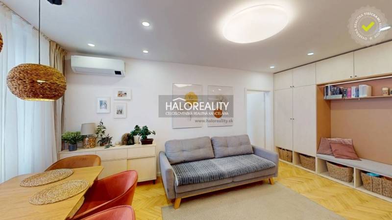 Nappali kanapéval, étkezőasztallal és fa mintázatú padlóval egy háromszobás lakásban.