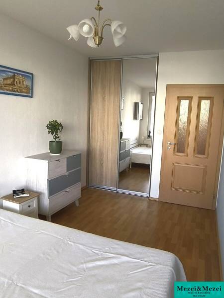 Hálószoba egy kétszobás lakásban fa dekorációjú padlóval, beépített szekrénnyel és komóddal.