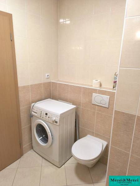 Fürdőszoba egy kétszobás lakásban világos csempékkel, mosógéppel és fali WC-vel.