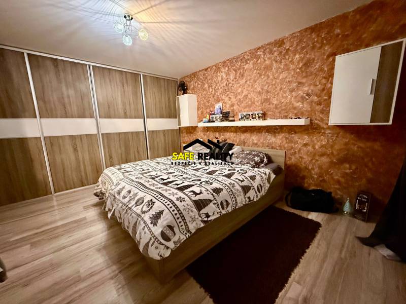 Hálószoba egy kétszobás lakásban ággyal, tárolóhellyel és fa dekorációjú padlóval.