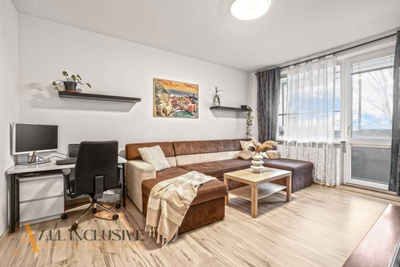 Nappali egy háromszobás lakásban kanapéval, íróasztallal és fa dekorációjú padlóval.