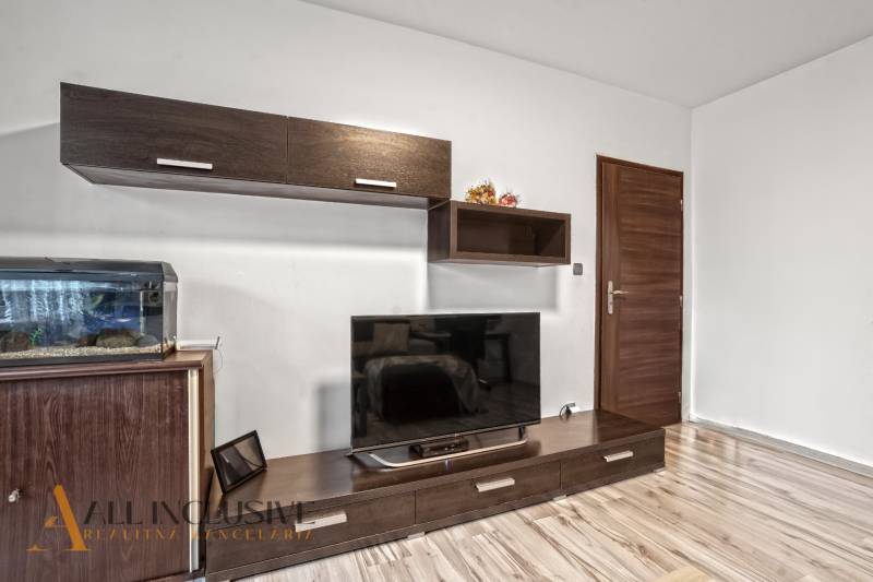 Nappali egy háromszobás lakásban, fa dekoros padlóval és nagy televízióval.