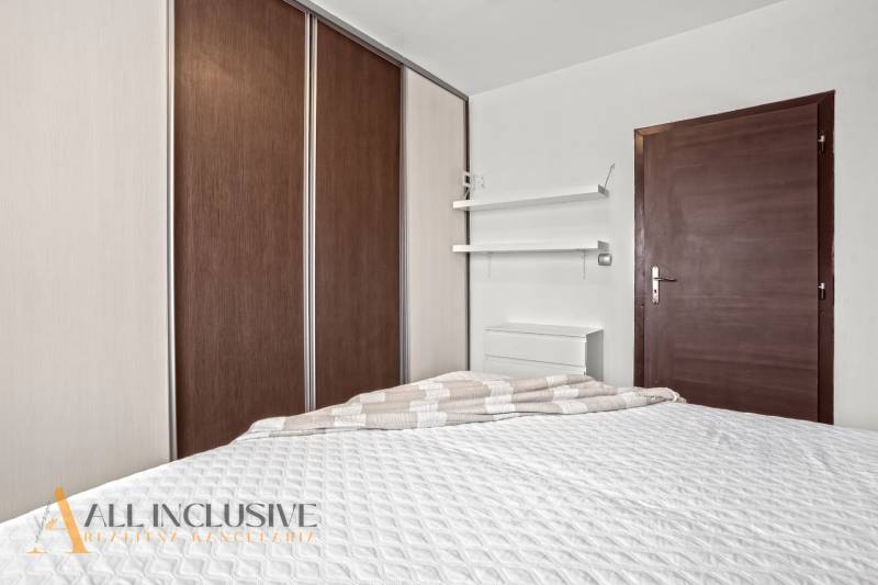 Hálószoba egy háromszobás lakásban ággyal, beépített szekrénnyel és minimalista polcokkal.