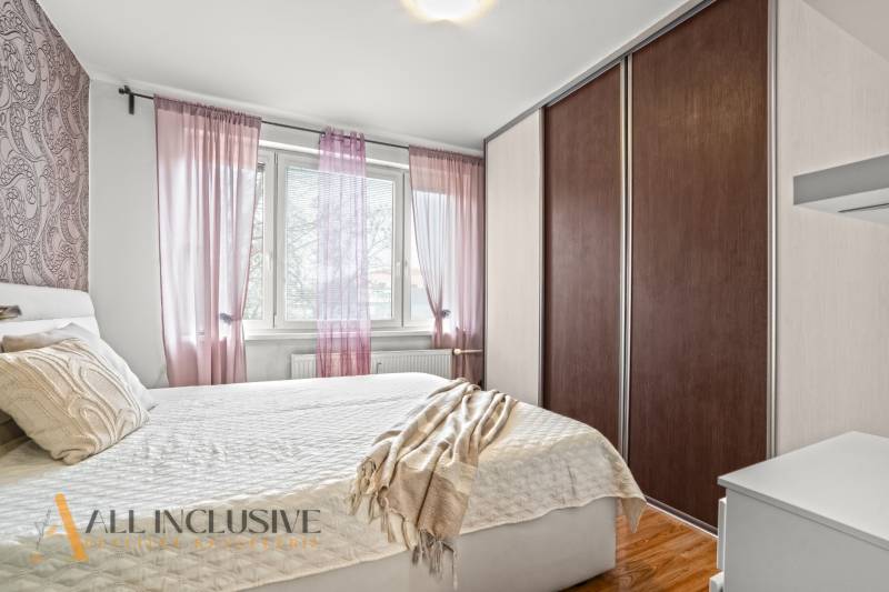 Hálószoba egy háromszobás lakásban ággyal, szekrénnyel és dekoratív párnákkal, fa dekoros padlóval.