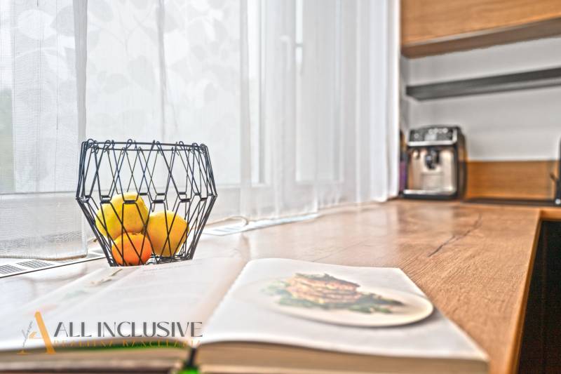 Nyitott konyha egy háromszobás lakásban fa dekorációval, gyümölcsöstál az asztalon.