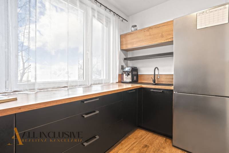 Konyha egy háromszobás lakásban nagy ablakkal, fekete szekrényekkel és fa dekoros padlóval.