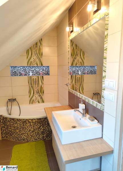 Családi ház fürdőszobája káddal, mosdóval, tükörrel és mozaik díszítéssel.