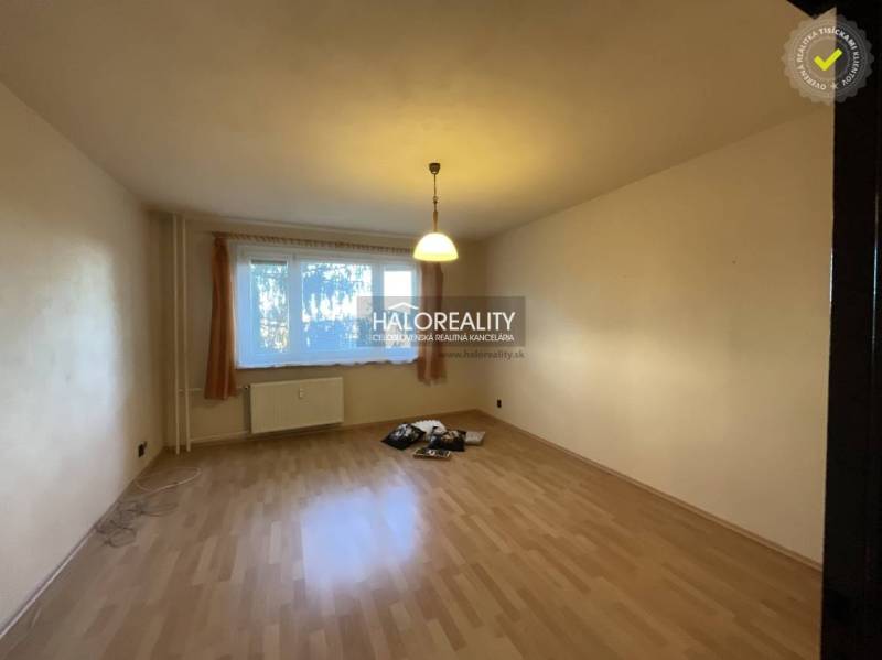 Nappali egy háromszobás lakásban, fa mintázatú padlóval és nagy ablakkal.