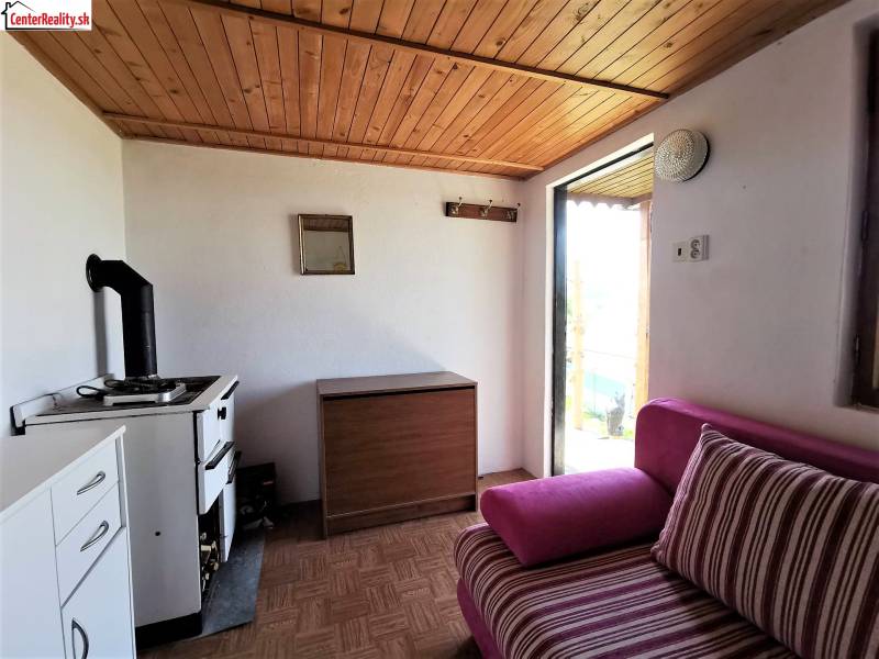 Egy hangulatos faházban van egy vintage tűzhely, fából készült mennyezet és kényelmes kárpitozott kanapé.