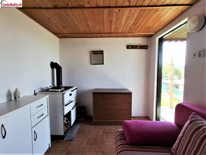 A konyhában van egy tűzhely, egy szekrény, egy rózsaszín kanapé és kilátás a kertre.