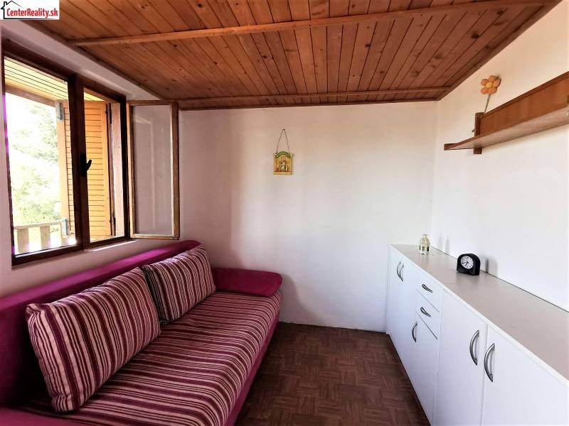 Fahmennyezetes, kényelmes kanapéval és fehér tárolóbútorokkal berendezett házikó.