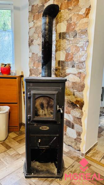 Kandalló kéménnyel, kőfal, fahatású padló egy faházban.