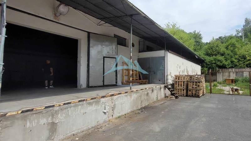 Raktárak és csarnokok a Vasúti utcában raklapokkal és tetővel, mellettük bokrok.