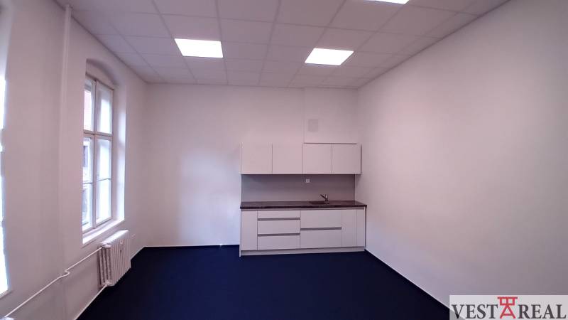 Irodák konyhasarokkal és kék szőnyeggel, fehér falakkal és nagy ablakkal.