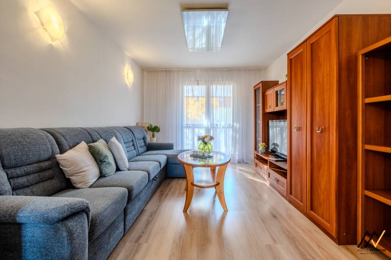 Nappali egy kétszobás lakásban, fa mintázatú padlóval, kényelmes kanapéval és bútorfallal.