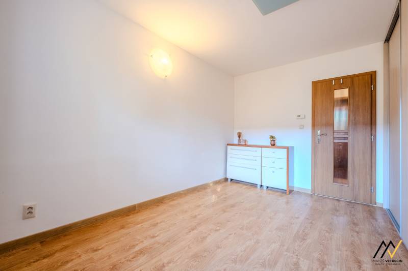 Szoba egy kétszobás lakásban fa dekor padlóval és fehér komóddal.