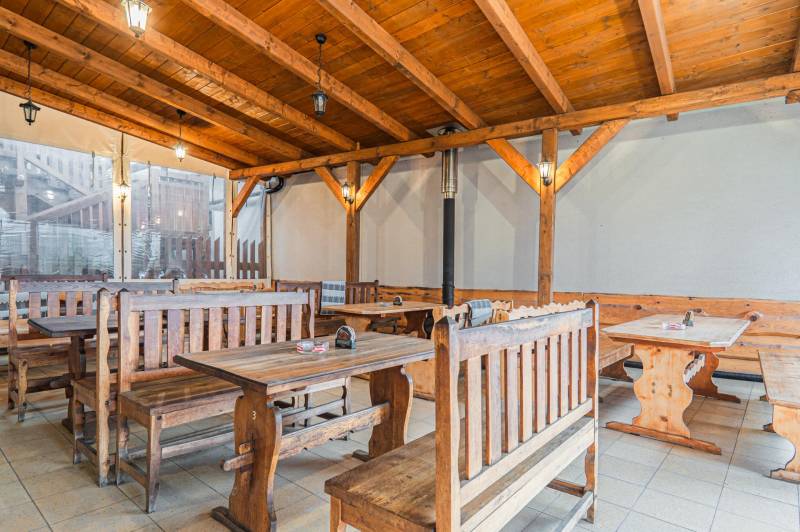Egy szállodai és panziós stílusú étterem belső tere fa padokkal és asztalokkal.
