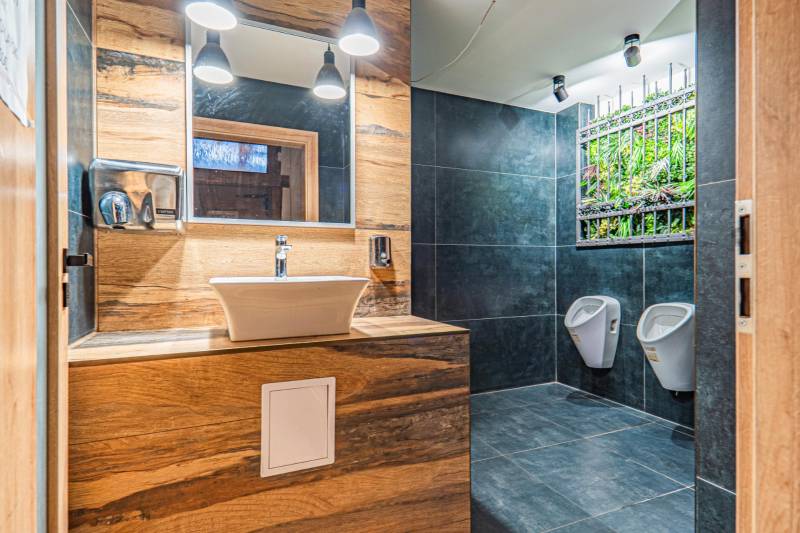 Fürdőszoba mosdóval, sötét csempével, függőleges kerttel és fa dekorációjú padlóval. Szállodák és panziók.