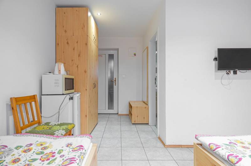 Panzió belső tere ágyakkal, televízióval, szekrénnyel, mikrohullámú sütővel és hűtőszekrénnyel.