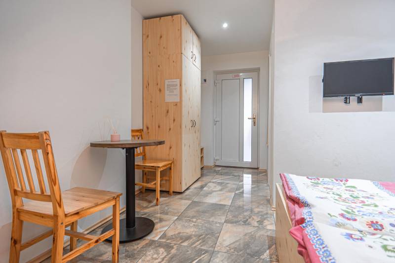 Szoba szállodákban és panziókban csempével, fa asztallal, székekkel, TV-vel és ággyal.