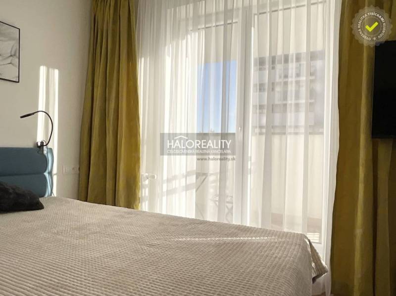 Világos hálószoba egy egyszobás lakásban nagy ablakkal és függönyökkel.