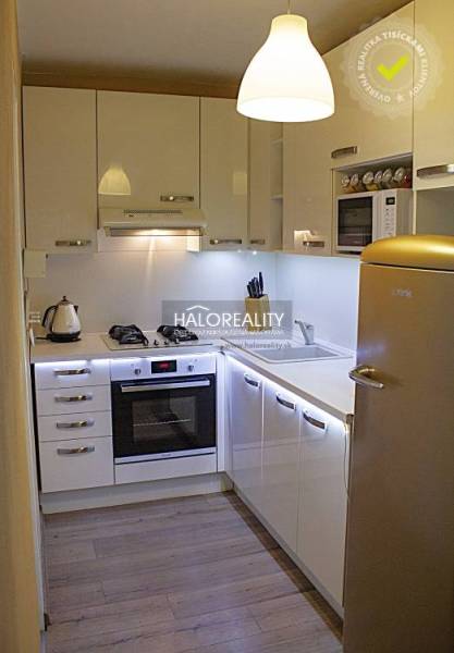 Konyha egy kétszobás lakásban fehér szekrényekkel és fa mintázatú padlóval.