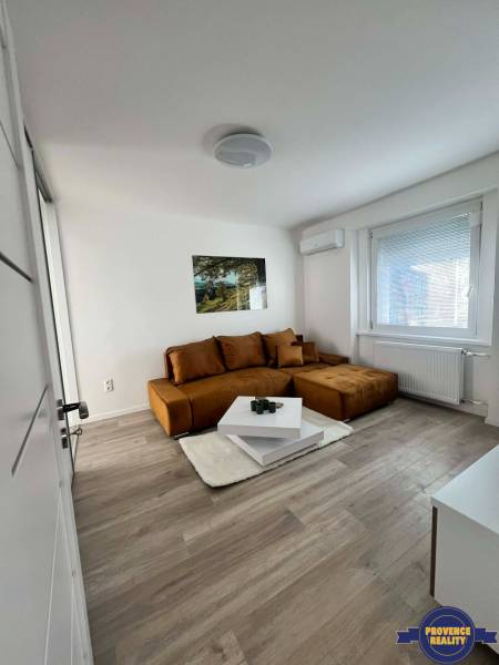 Világos nappali egy kétszobás lakásban barna kanapéval és asztallal fa dekor padlón.