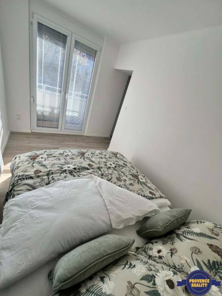 Világos hálószoba egy kétszobás lakásban dekoratív párnákkal és fa dekorációjú padlóval.